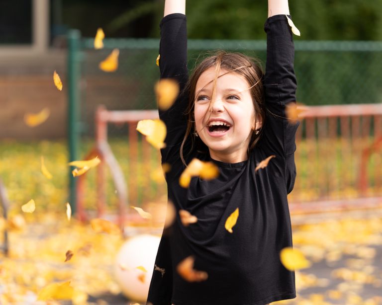 Happy smiling girl with shaggy brown hair in black shirt playing with autumn foliage at daytime